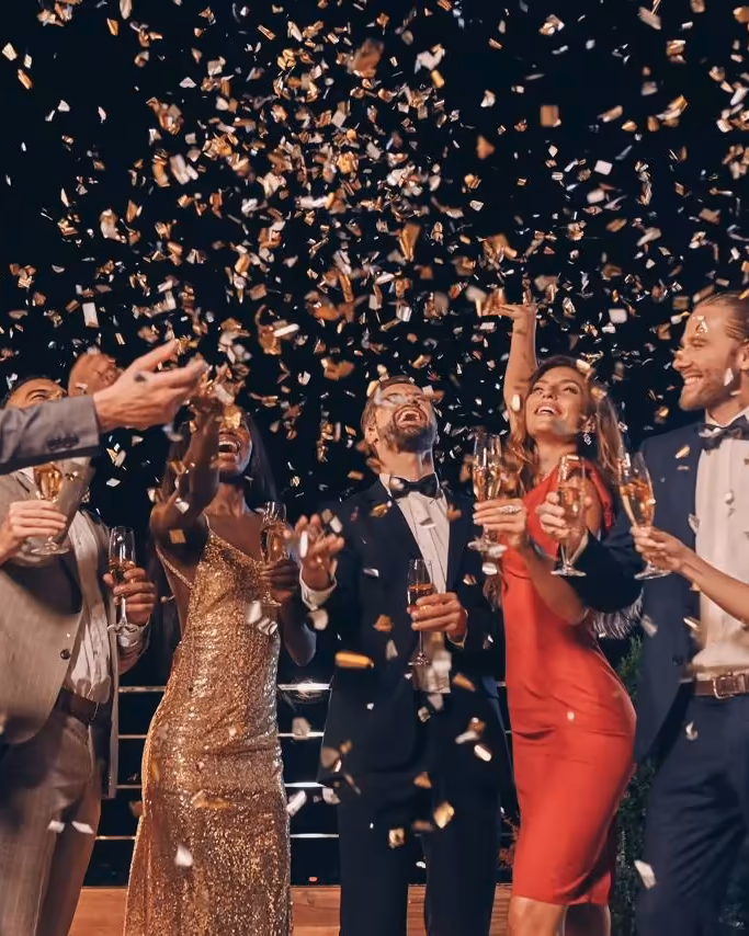 Guests in black tie raising champagne glasses beneath falling gold confetti at an awards evening